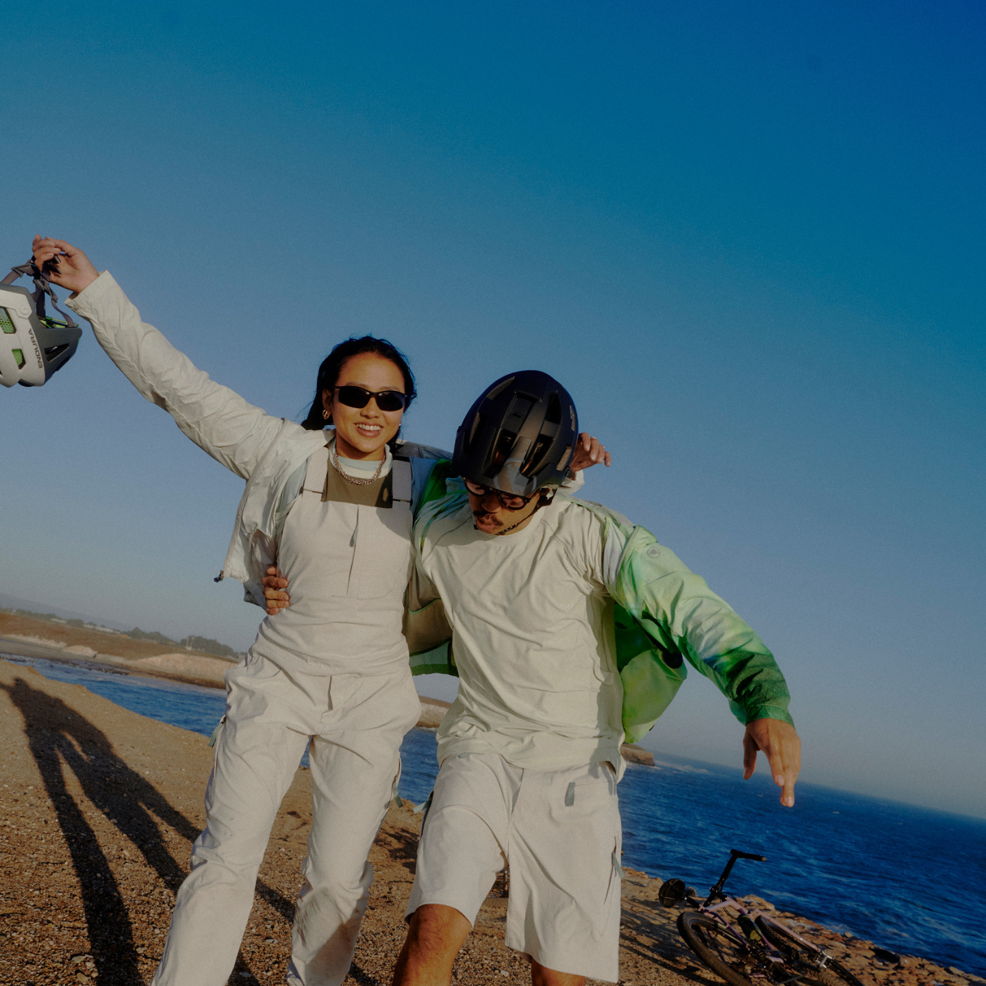 Two people in light clothing standing on a beach with clear blue skies.