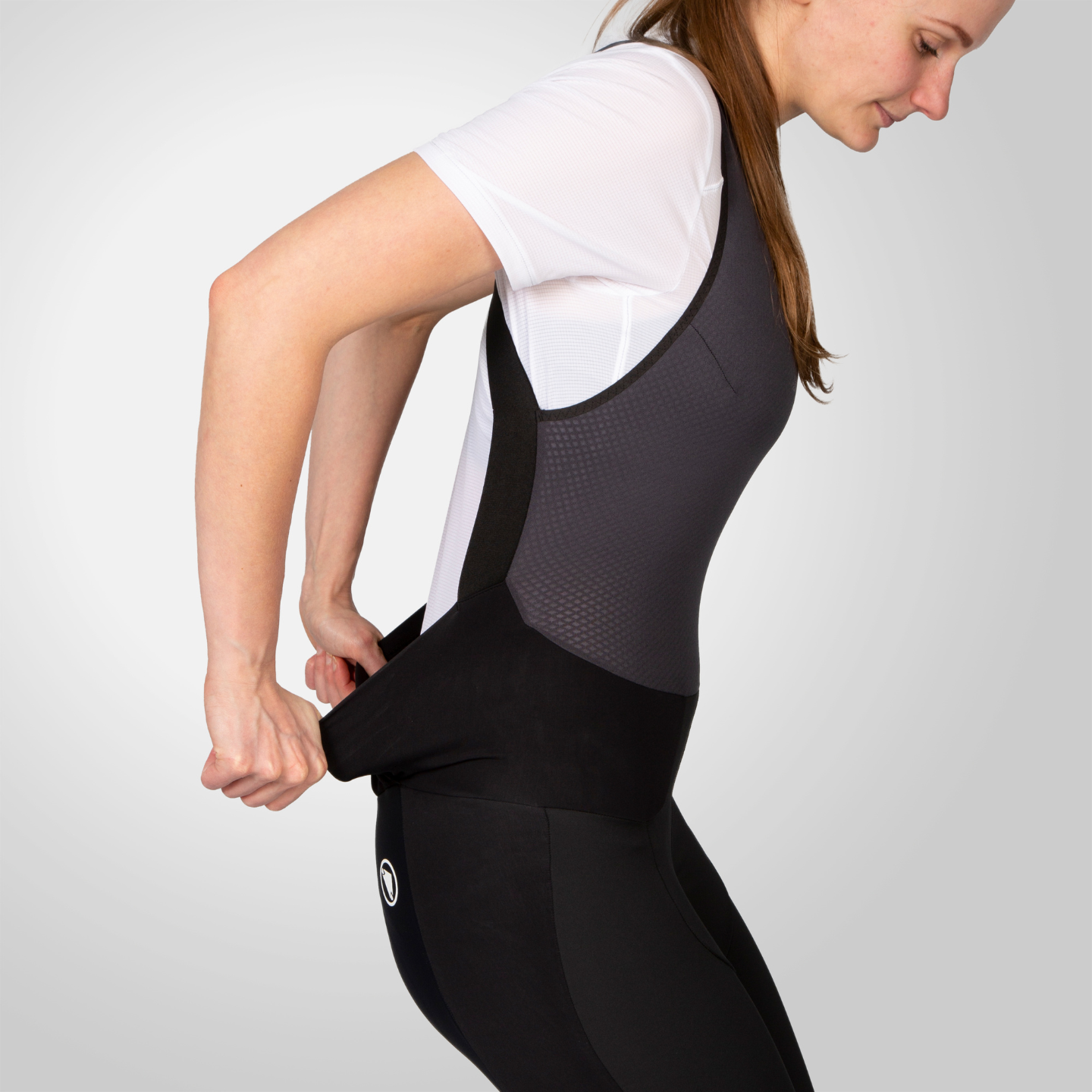Woman wearing a black cycling bib shorts with dropseat feature on a plain background